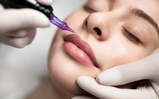 Permanent makeup artist applying lip blush pigment with a PMU machine during a cosmetic procedure