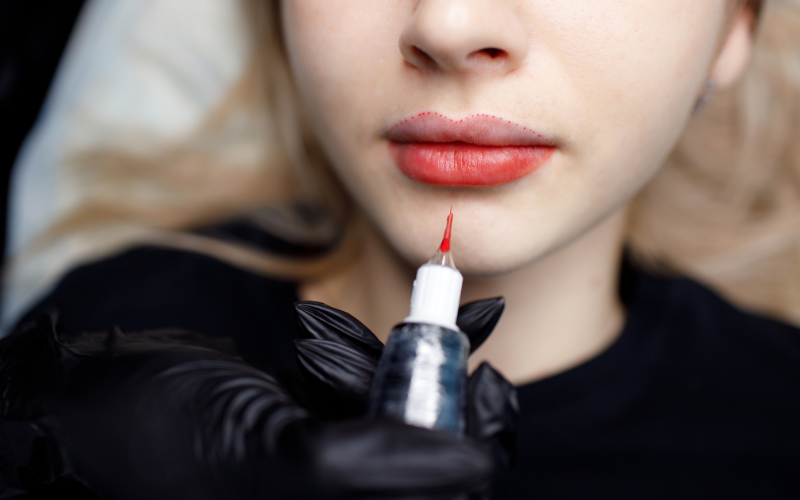 Permanent makeup artist preparing to tattoo lips, with outline marks visible on the client’s lip border