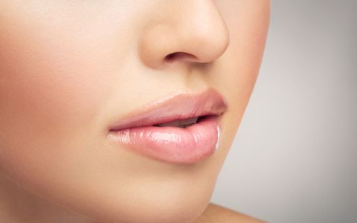 A close-up of a woman's smooth, glossy, light pink lips and flawless skin