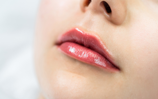 A close-up shot from a low angle of a woman's full, glossy, rosy-pink lips after a cosmetic enhancement